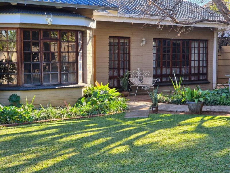 A view of the rear facade featuring a bay window, timber-framed windows, and french doors opening onto a paved walkway and garden area.