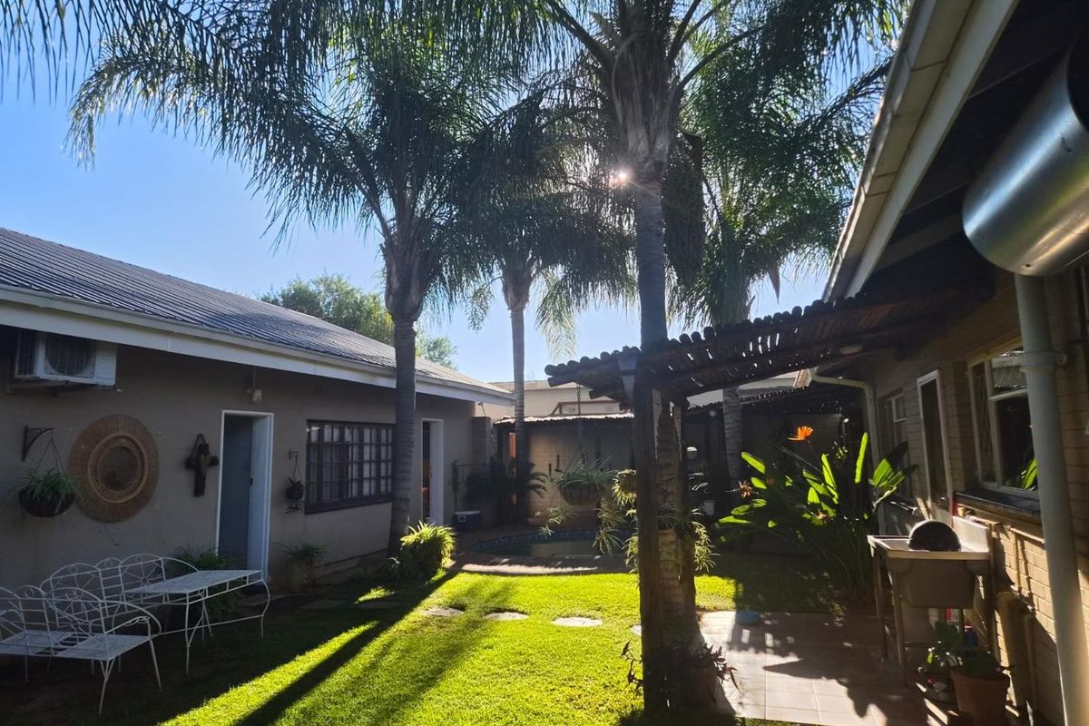 A well-maintained rear garden area featuring a lawn, mature palm trees, a covered patio with a pergola, and an external utility wash basin.