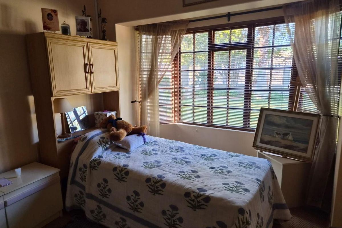 A cozy bedroom featuring built-in cabinetry and a large bay window with venetian blinds, providing ample natural light.