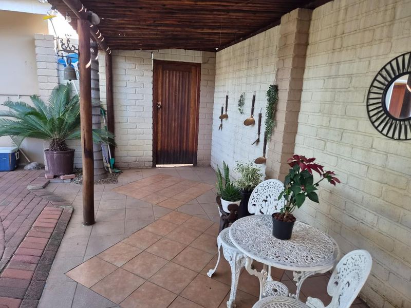 A covered patio area featuring tiled flooring, painted brick walls, and a timber pergola structure, providing a functional outdoor living space.