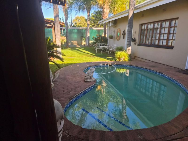 A private backyard featuring a swimming pool with brick paving, a timber pergola, and a well-maintained lawn area.