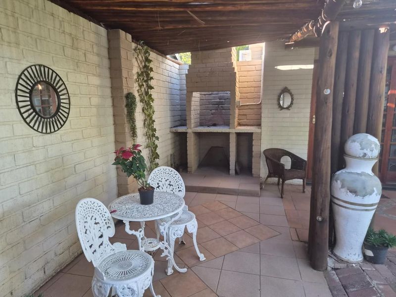 Covered outdoor patio featuring a built-in brick braai, tiled flooring, and a timber pergola roof, ideal for relaxed outdoor entertaining.
