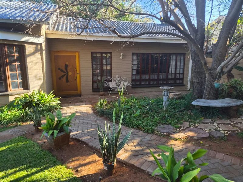 Front entrance of the house featuring a brick facade, paved walkway, and established garden area with mature trees.