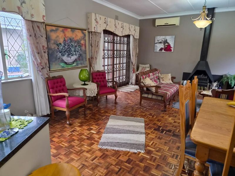 Open-plan living and dining area featuring classic parquet flooring, a built-in fireplace, and direct access to the exterior through a security gate.