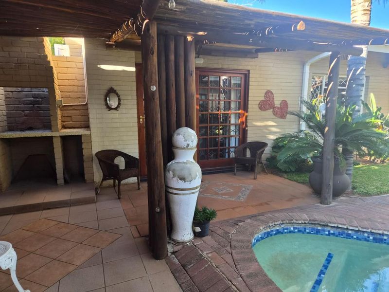 Covered outdoor patio area featuring a built-in braai, timber pergola structure, and direct access to the swimming pool and garden.