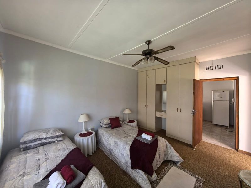 A bedroom featuring built-in cupboards, a ceiling fan, and carpeted flooring, with an adjacent room visible through the doorway.