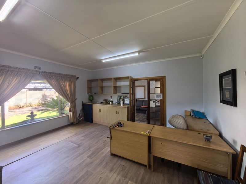 A functional home office featuring laminate flooring, built-in cabinetry with shelving, and natural light through a large window.