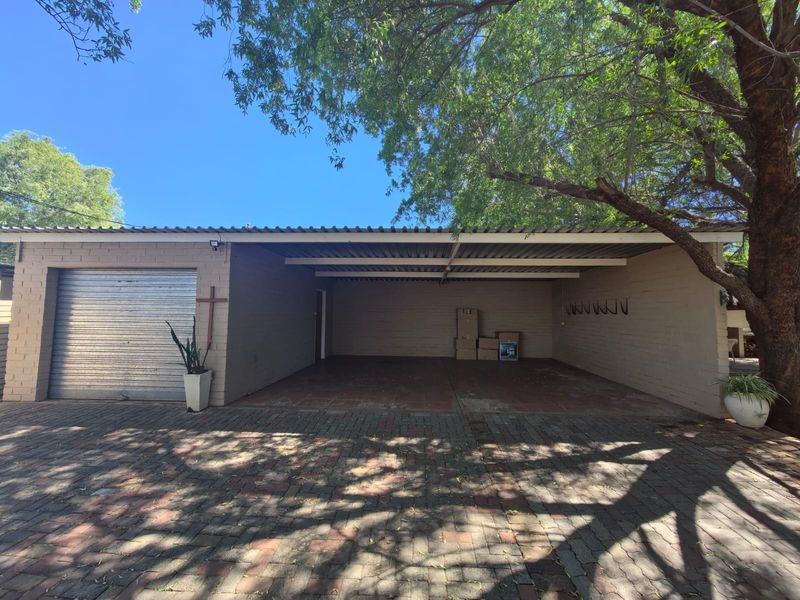 A spacious double carport and enclosed garage area featuring brick paving, exposed brick walls, and a corrugated metal roof structure.