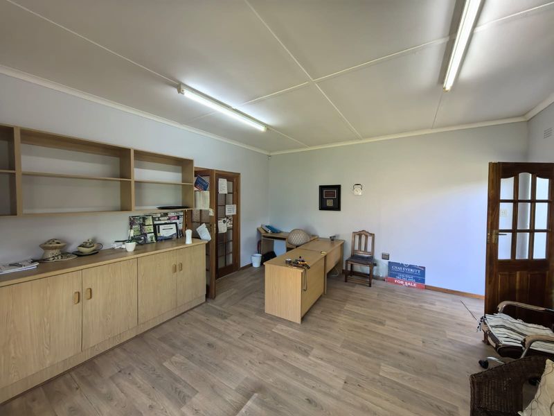 A functional office space featuring laminate flooring, built-in storage cabinetry, and fluorescent lighting, suitable for a home workspace or study.