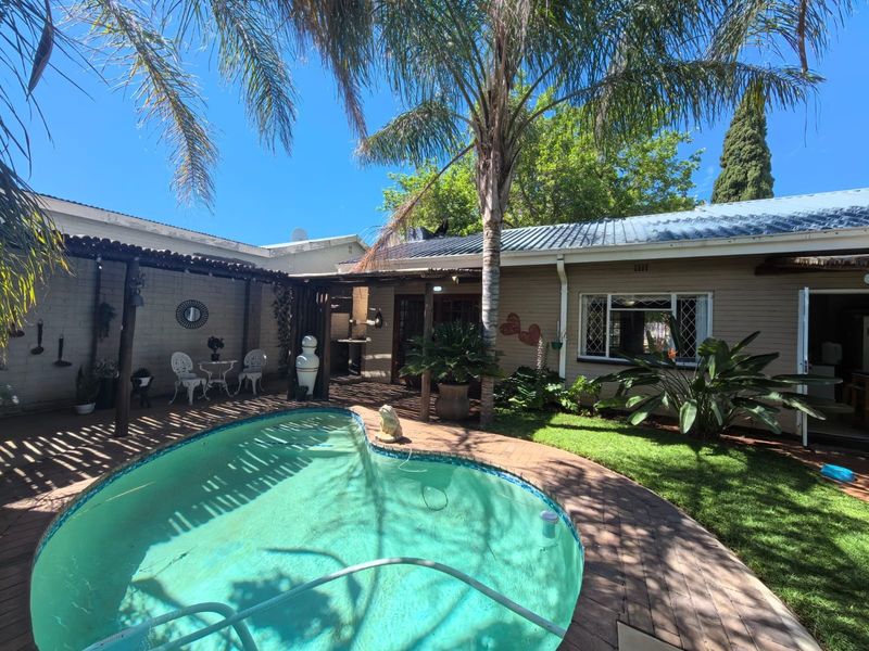 Outdoor pool area featuring a swimming pool, brick paving, and a timber pergola, set within a landscaped garden with mature trees.