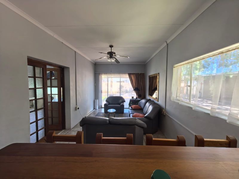 A functional living room featuring a ceiling fan, tiled flooring, and access to the outdoors through a sliding glass door and timber-framed glass door.