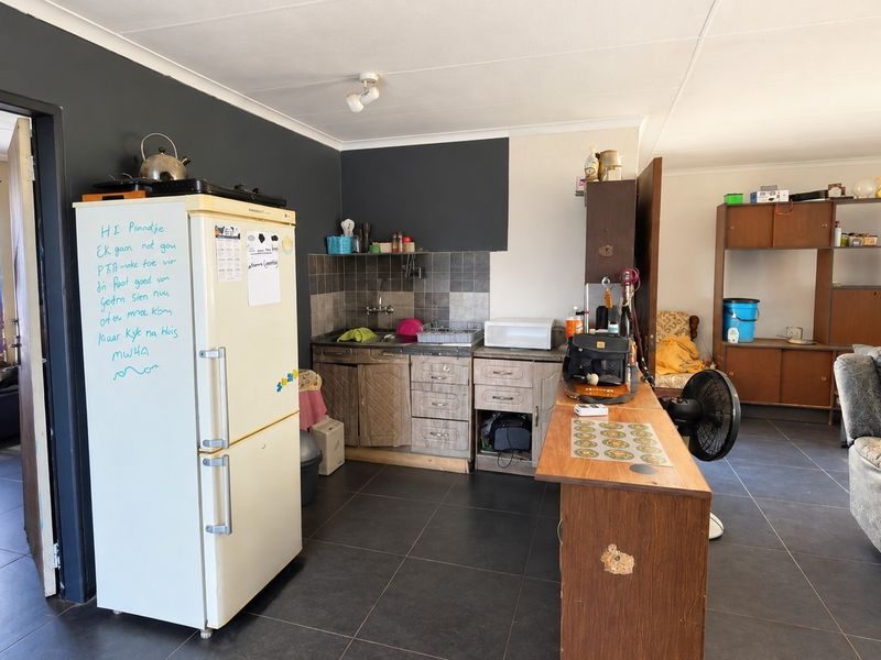 Open-plan living area featuring a compact kitchen with tiled backsplash and dark floor tiles, offering a functional layout for modern living.