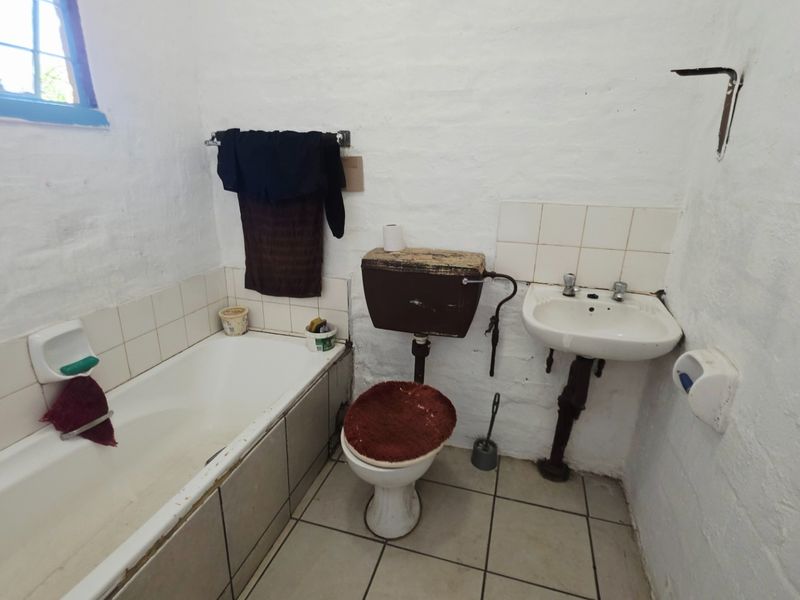 A dated bathroom featuring a bathtub, toilet, and washbasin with visible wear and exposed plumbing, requiring renovation to modernize the space.