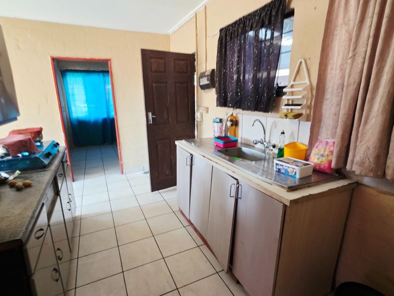 A functional kitchen area featuring tiled flooring, basic cabinetry, and a stainless steel sink, offering potential for modernization and cosmetic updates.