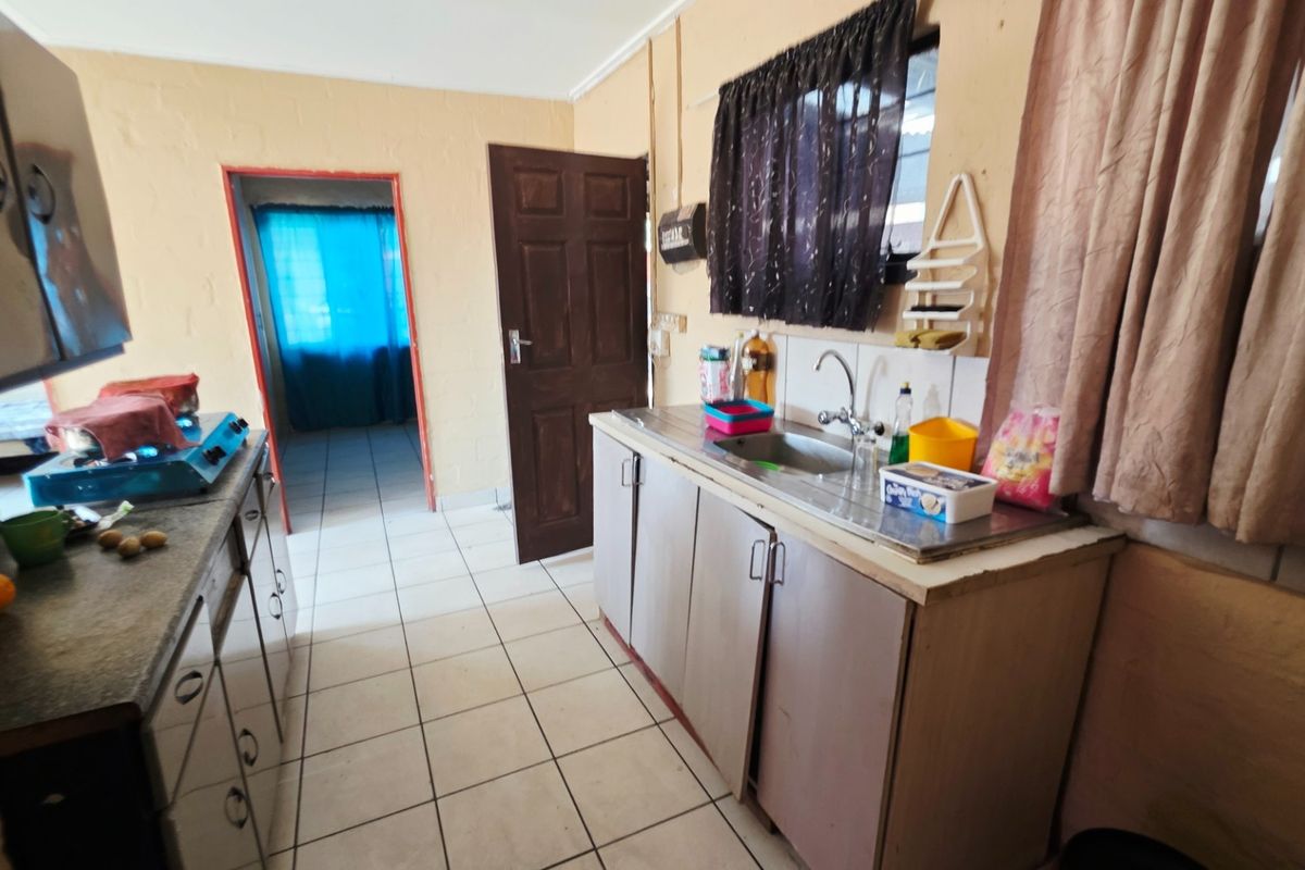 A functional kitchen area featuring tiled flooring, basic cabinetry, and a stainless steel sink, offering potential for modernization and cosmetic updates.