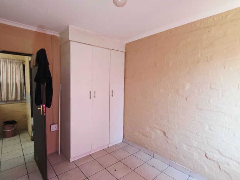A vacant bedroom featuring tiled flooring, a built-in wardrobe, and an exposed brick wall, offering a blank canvas for renovation.