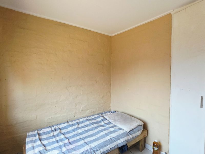 A compact bedroom featuring tiled flooring, textured walls, and a built-in wardrobe.