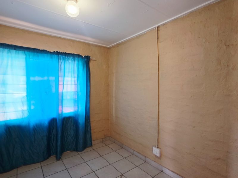 A vacant bedroom featuring tiled flooring, built-in cupboards, and textured wall finishes with surface-mounted electrical conduit.