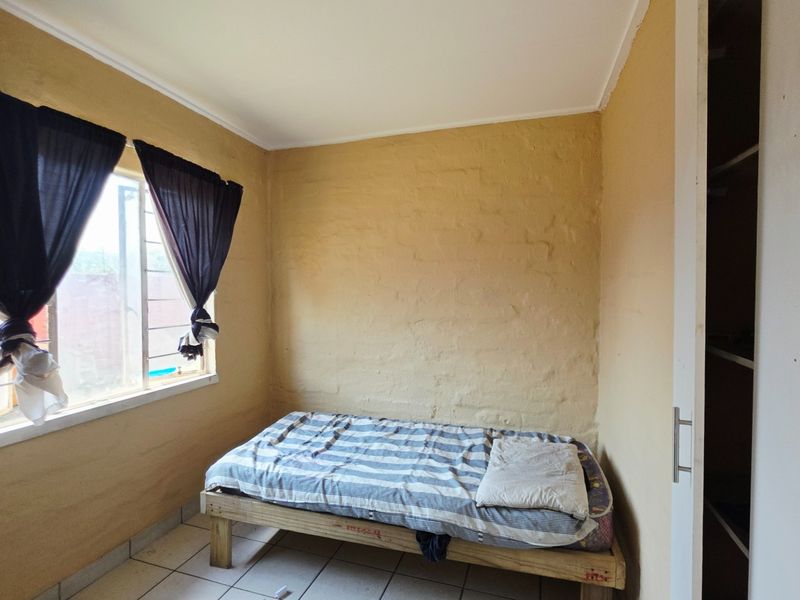 A bedroom featuring tiled flooring, a built-in cupboard, and an aluminium window frame, requiring cosmetic updates to the wall finishes.