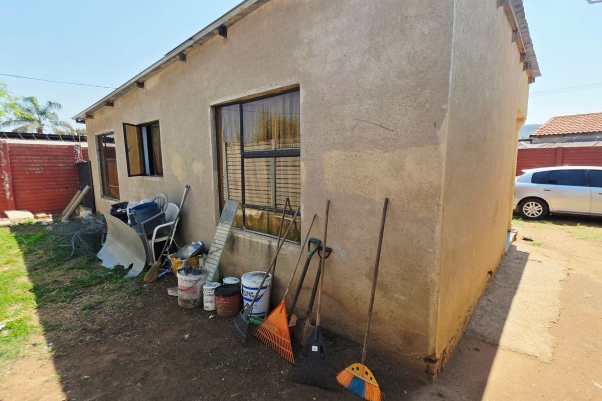 Rear exterior view of the property featuring plastered walls, metal window frames, and a corrugated roof, requiring maintenance and landscaping.