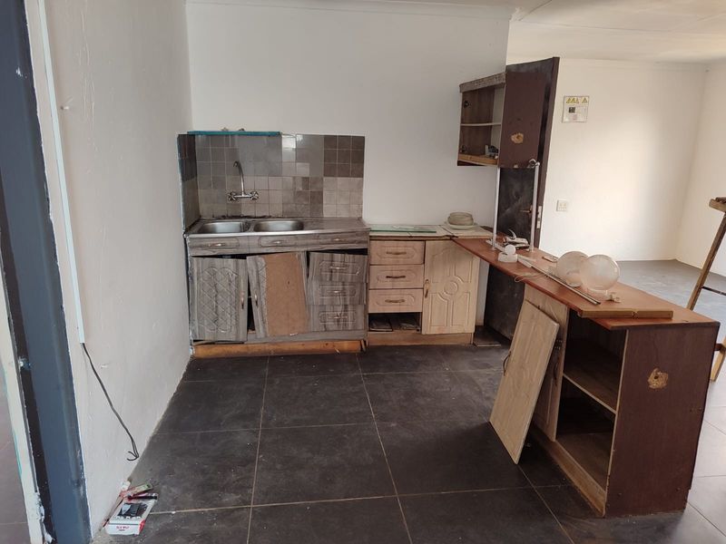 A small, dated kitchen area featuring a double bowl sink, tiled splashback, and worn built-in cabinetry in need of renovation.