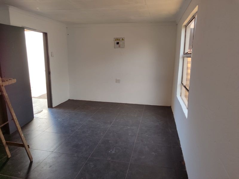 A vacant, neutrally finished room featuring dark tiled flooring, a window, and an accessible electrical distribution board.