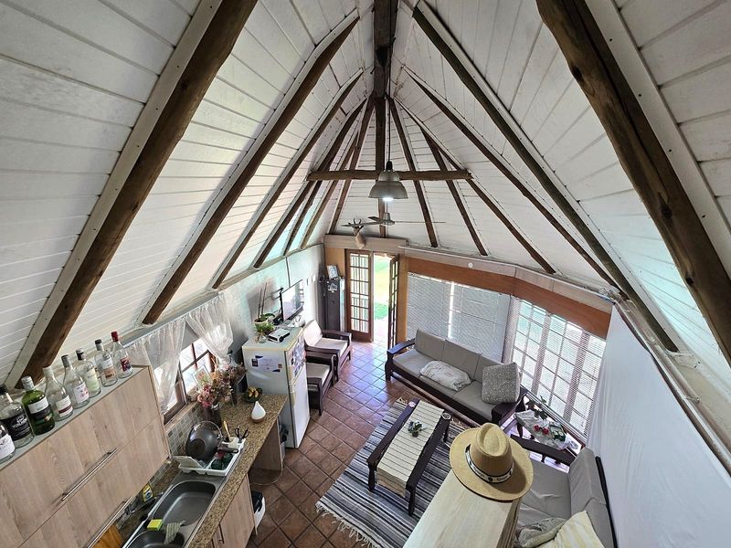 Open-plan living area featuring a high vaulted timber ceiling with exposed rafters, tiled flooring, and integrated kitchen cabinetry with direct access to the outdoors.