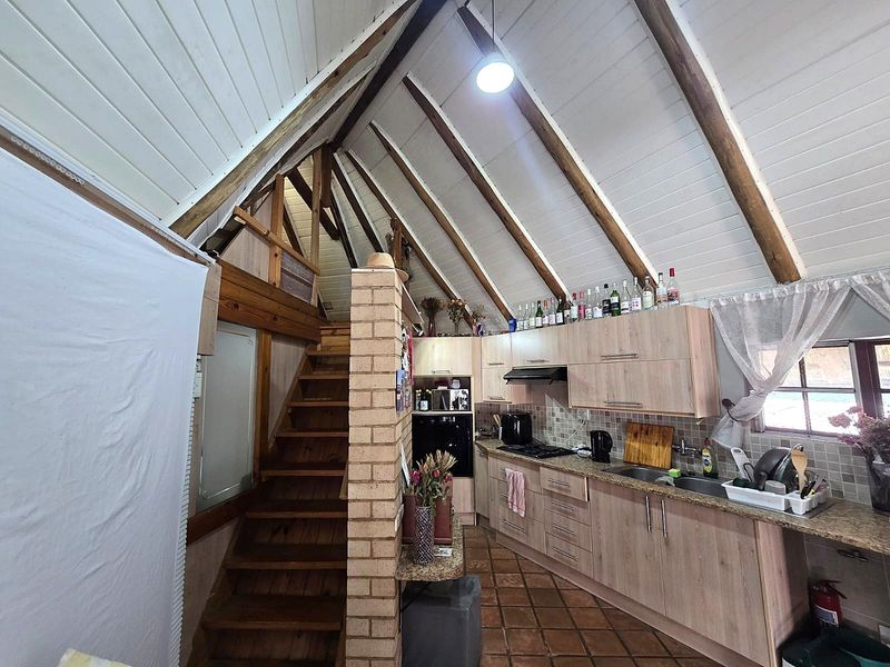 Open-plan kitchen and living area featuring a vaulted ceiling with exposed timber rafters, a brick feature wall, and a timber staircase to a mezzanine level.