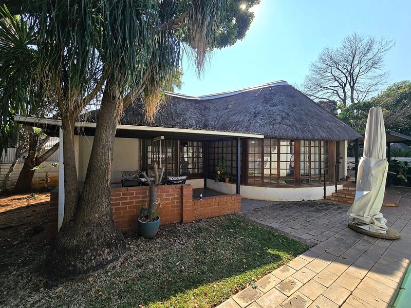 Rear view of a cottage featuring a traditional thatch roof, a covered patio area with a brick wall, and timber-framed windows overlooking the garden.
