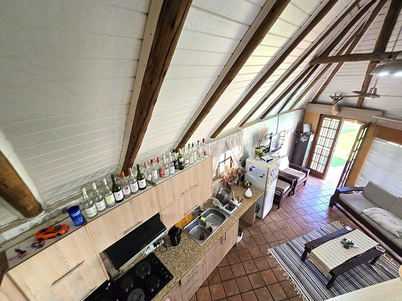 Open-plan living area featuring a vaulted timber ceiling with exposed beams, tiled flooring, and a functional kitchen with granite countertops and built-in cabinetry.