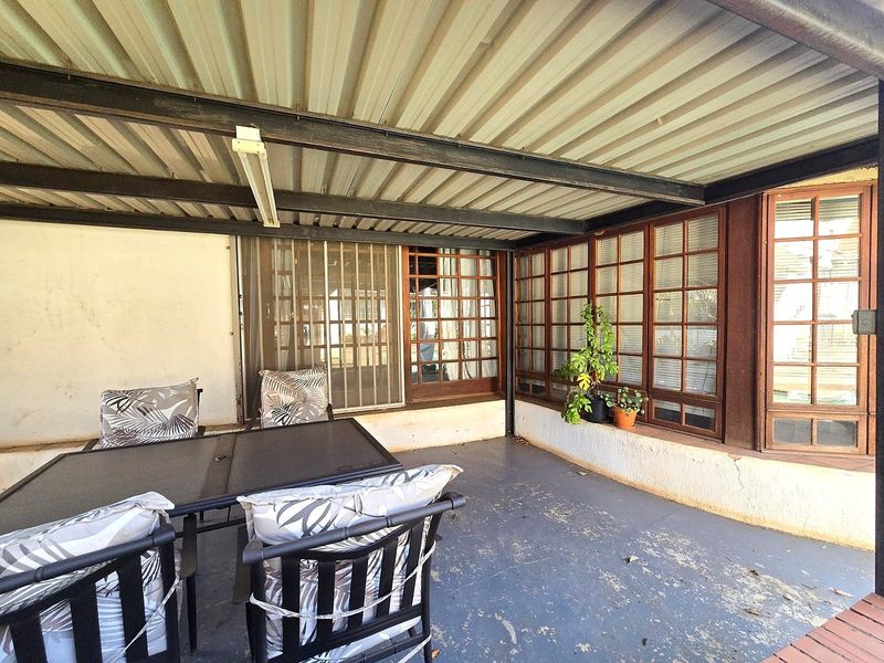 A covered outdoor patio area featuring a corrugated metal roof, steel beams, and timber-framed windows, requiring some maintenance to the flooring and wall finishes.