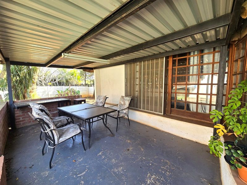 A covered outdoor patio area featuring a corrugated metal roof, steel structural beams, and a brick retaining wall, providing a functional space for outdoor living.