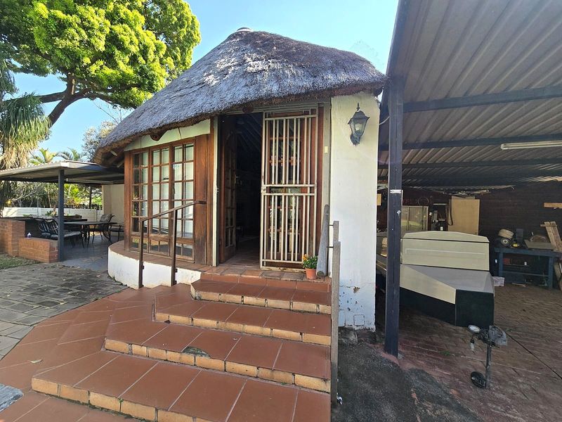 Rear view of a cottage featuring a traditional thatch roof, tiled entrance steps, and an adjacent carport structure.