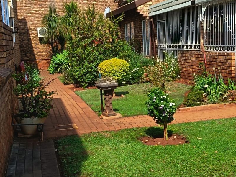 A well-maintained rear garden area featuring brick paving, established landscaping, and secure window bars on the brick building exterior.