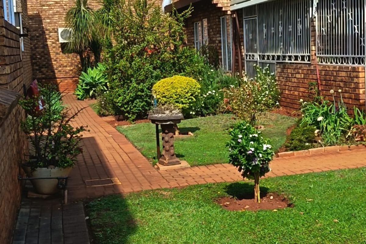 A well-maintained rear garden area featuring brick paving, established landscaping, and secure window bars on the brick building exterior.
