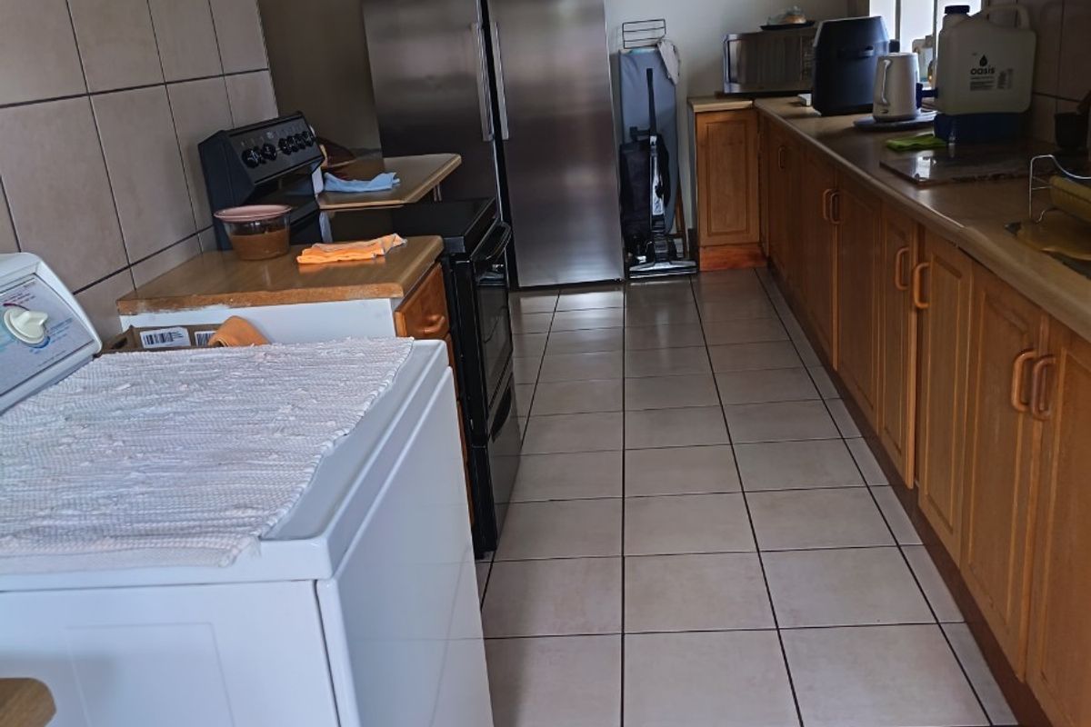 A functional kitchen featuring wooden cabinetry, tiled flooring, and a tiled splashback, offering a practical layout for daily use.