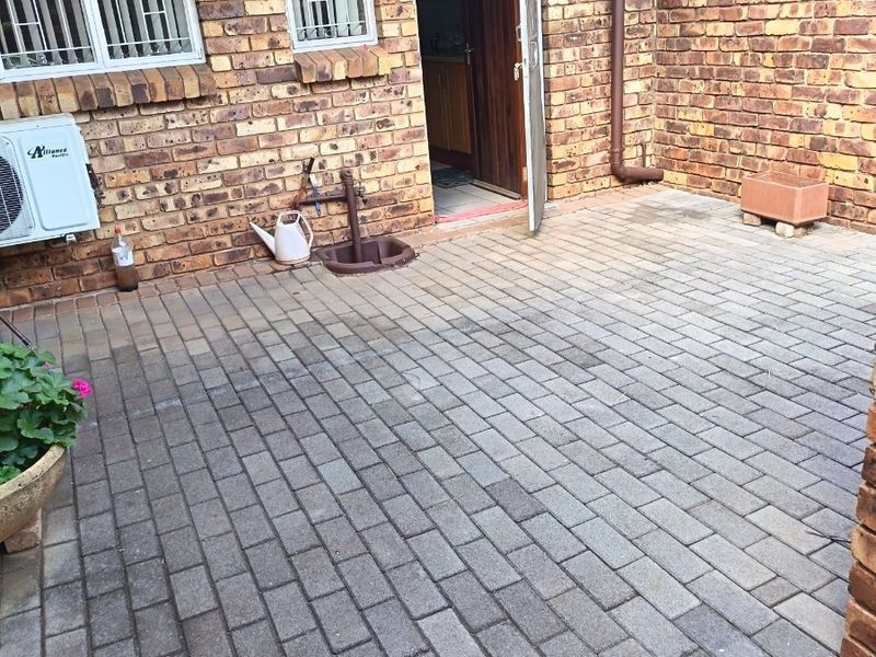 A paved outdoor patio area featuring face brick walls, an external water tap, and an installed air conditioning unit.