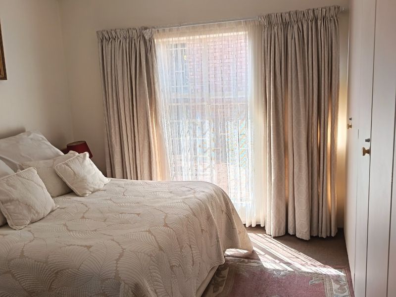 A functional bedroom featuring built-in cupboards and large windows with curtain tracks, providing natural light and storage space.
