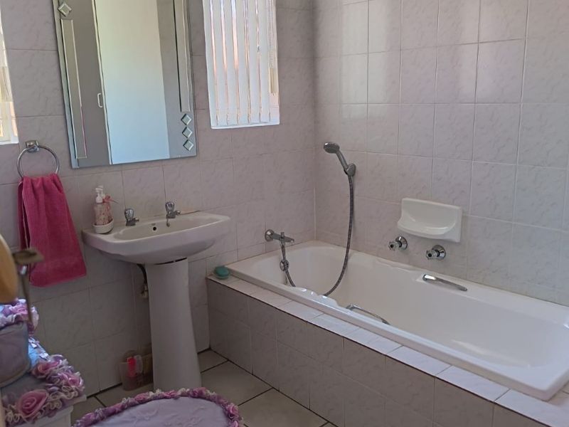 A functional bathroom featuring a pedestal basin, a built-in bathtub with a handheld shower mixer, and fully tiled walls and flooring.