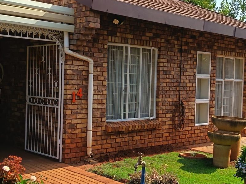 Front elevation of a retirement village unit featuring face brick construction, a tiled roof, paved walkway, and secure entrance gate.