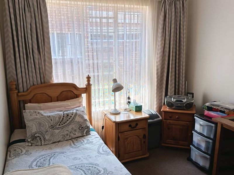 A cozy bedroom featuring carpeted flooring and a large window with installed curtain tracks, providing natural light to the space.