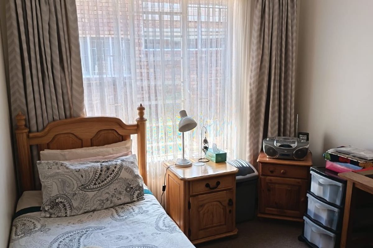 A cozy bedroom featuring carpeted flooring and a large window with installed curtain tracks, providing natural light to the space.