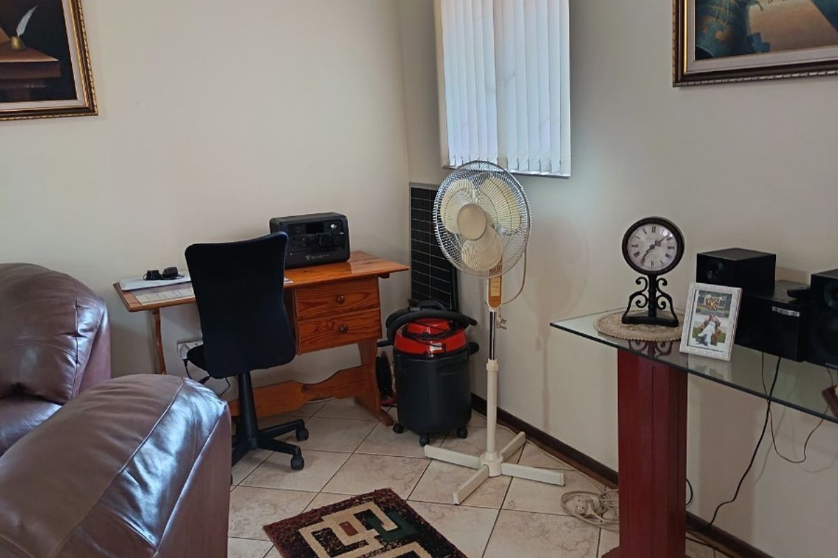 A living area featuring ceramic floor tiles, vertical blinds, and a wall-mounted air conditioning unit, providing a functional and neutral space.