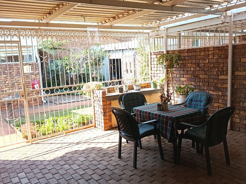 A covered outdoor patio featuring brick paving, a face brick wall, and a built-in brick counter, enclosed by a secure wrought iron gate.