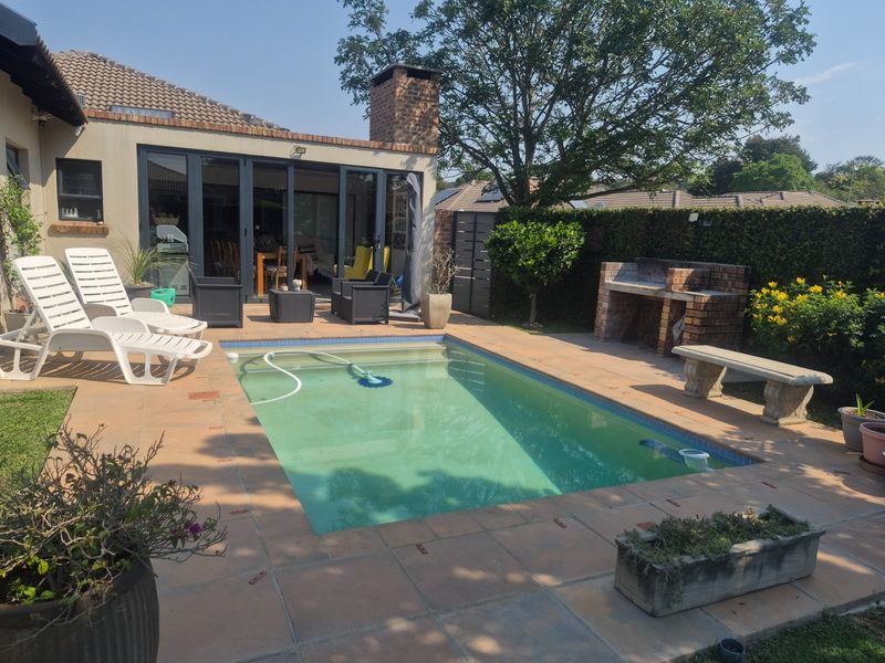 Outdoor pool area featuring a tiled patio, built-in brick braai, and direct access to the home through large bi-fold doors.