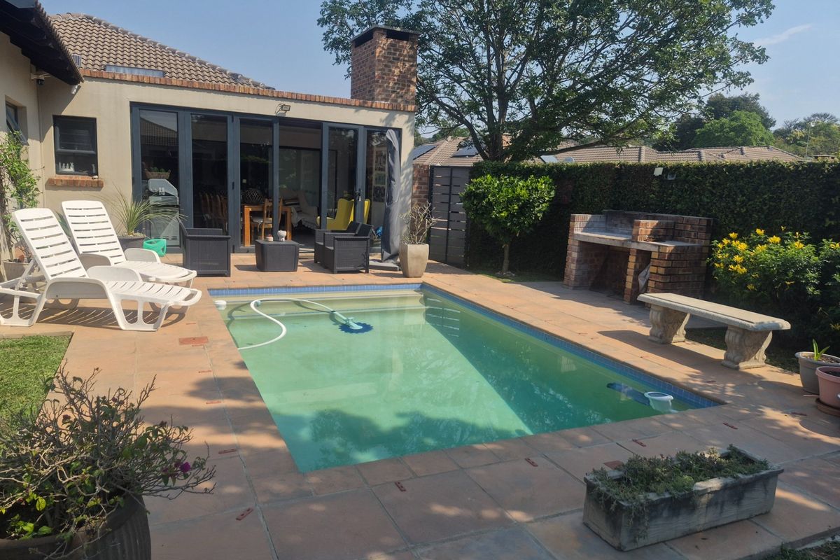 Outdoor pool area featuring a tiled patio, built-in brick braai, and direct access to the home through large bi-fold doors.