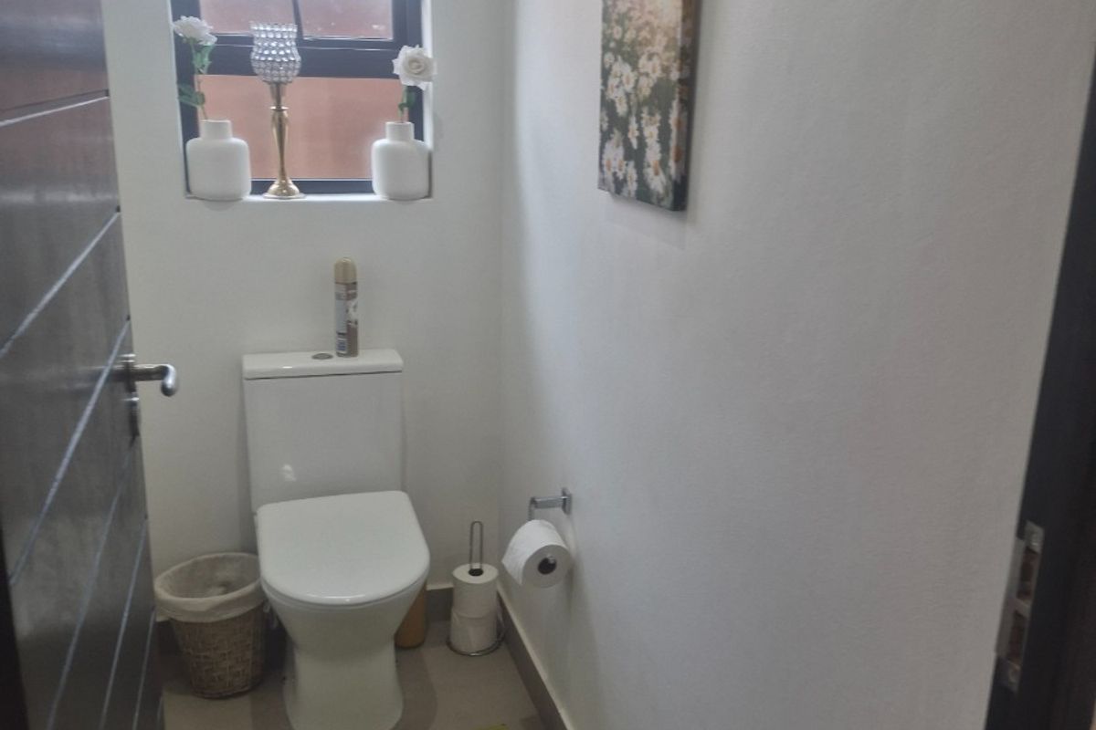 A compact guest bathroom featuring tiled flooring, a modern toilet, and a window with security bars.
