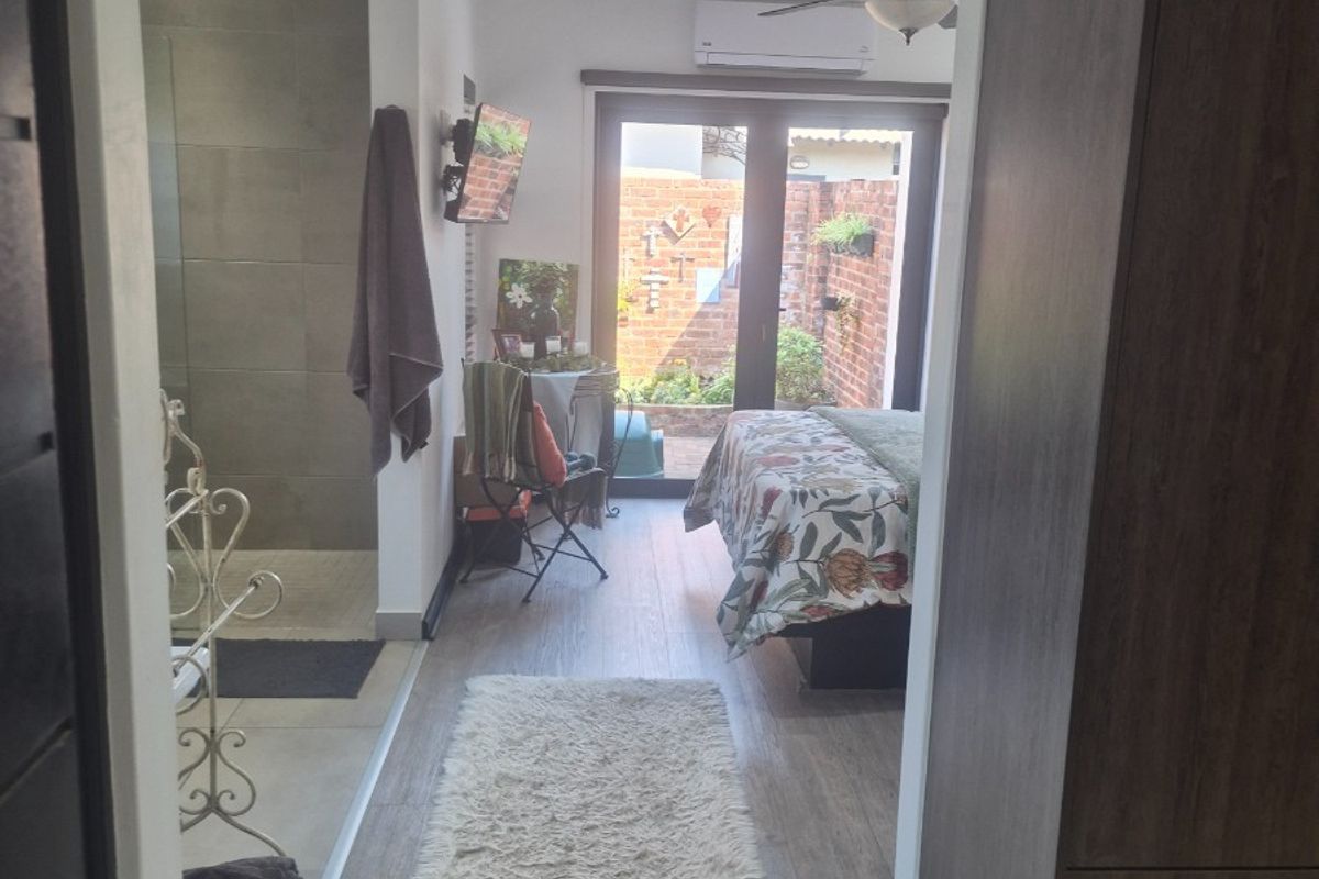 A modern bedroom featuring laminate flooring, built-in cupboards, an en-suite shower area, and direct access to a private outdoor courtyard through sliding glass doors.