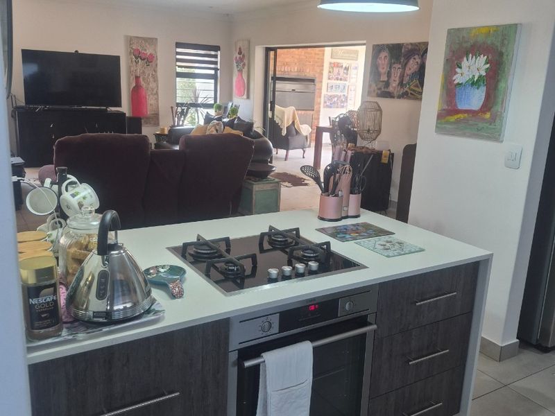 Open plan kitchen featuring a central island with built-in gas hob and oven, flowing into a spacious living area with access to the patio.