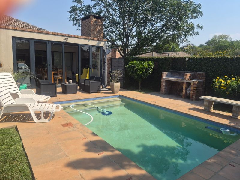 Outdoor pool area featuring a built-in brick braai, tiled patio, and direct access to the home through large stacking doors.